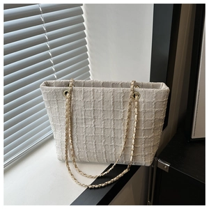 Detail of beige tweed tote bag with gold chain strap in a sunny minimalist interior