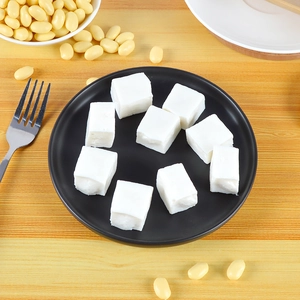 Macro detail of nine miniature tofu food models on a black plate with soy beans decoration