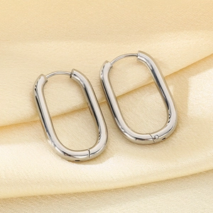 Macro view of silver oval stainless steel hoop earrings on beige silk fabric