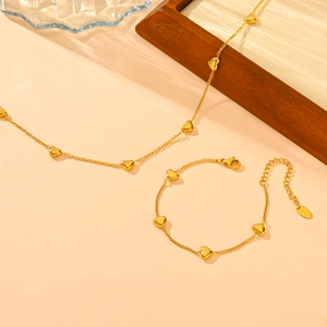 Detailed view of gold multi-heart necklace and bracelet set on a rustic wooden tray