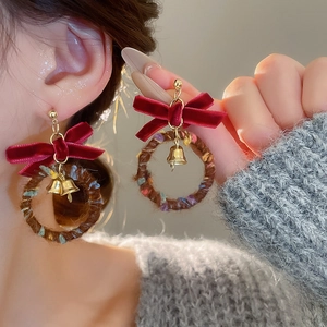Close-up of Christmas stud earrings with red velvet bow, brown wreath and gold bell