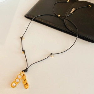 Détail du pendentif cosse de pois dorée avec perles blanches et cordon noir minimaliste