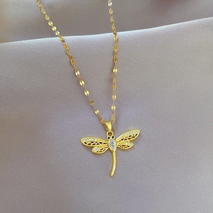 Close-up of golden dragonfly pendant necklace with zircon stones on gray fabric
