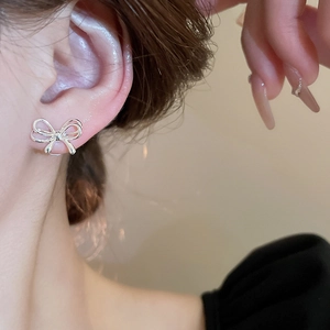 Close-up of minimalist silver bow stud earrings on model ear with polished metal finish
