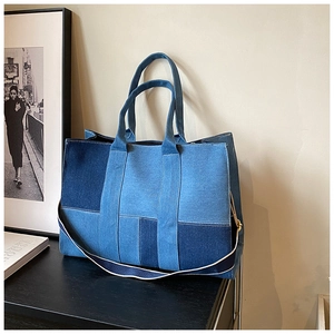 Detail of a patchwork denim tote bag with dual handles and detachable strap on a desk