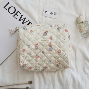 Détail d'une trousse de maquillage matelassée aux motifs lapin et nœud sur tissu blanc