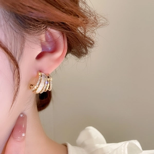 Detail of layered gold earrings with pavé crystals and mother-of-pearl inlays