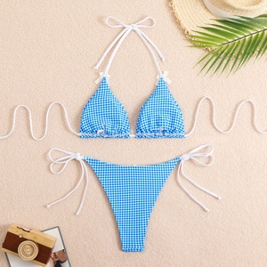 Flat lay of blue and white gingham bikini with bows and beach props on beige sand