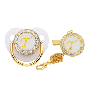 Detail of white pacifier and golden clip set with letter T and rhinestone accents