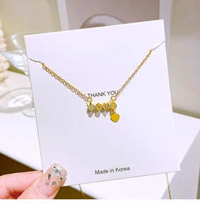 Close-up of gold LOVE pendant with crystal inlay and heart tassel on jewelry card