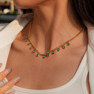 Detail of a gold necklace with teardrop green gemstones on a model in natural light