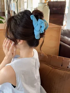 Detail view of a sky blue pleated fabric hair scrunchie on a brown updo hairstyle