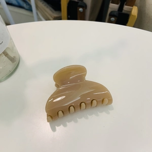 Close-up of a beige polished heart-shaped hair claw clip with teeth on a white table