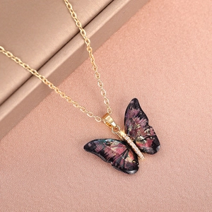 Macro detail of acrylic butterfly pendant with purple tint and gold chain for layering