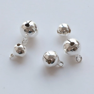 Flat lay of polished silver metal bells in various sizes with hanging loops on white background