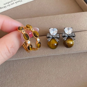 Detail view of gold-plated tiger eye stone earrings with zircon on a velvet tray