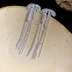 Silver bow tassel drop earrings with sparkling rhinestones on a ceramic display tray