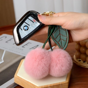 Detail of pink faux fur cherry keychain attached to a BMW car key held by a hand