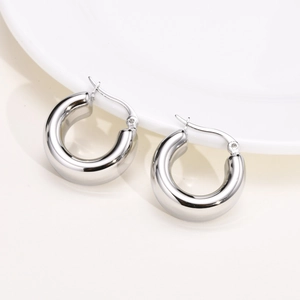 Detailed shot of small polished silver stainless steel hoop earrings on a white plate