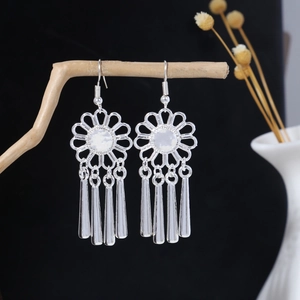 Close-up of vintage silver sunflower earrings with long fringe hanging on a wood branch