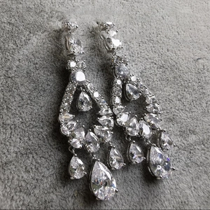 Macro shot of silver-tone drop earrings featuring multi-layered zircon stones on grey velvet