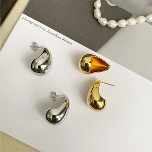Detailed view of teardrop metal stud earrings in polished gold and silver finishes