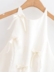 Detail shot of white top featuring delicate bow decorations on smooth silk-like fabric
