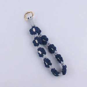 Detail of hand-woven daisy patterned keychain with navy cotton rope and gold clasp