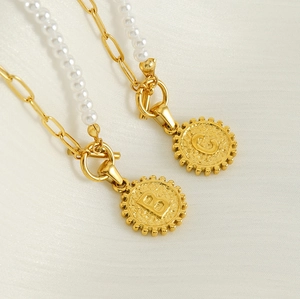 Detailed shot of two gold necklaces featuring OT buckle, pearls and initial B and G pendants
