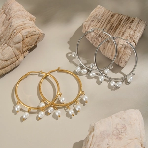 Detailed shot of large gold and silver hoop earrings with white pearl pendants on rocks