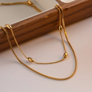 Elegant gold oval bead necklace with layered box chain design on dark wood tray