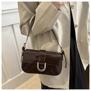 Detail of a dark brown patent leather bag with a golden horseshoe buckle on a model