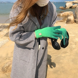 Outdoor shot of green knitted gloves worn by a model in a natural seaside setting