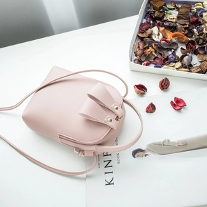 Pink mini crossbody bag in matte PU leather on white table with dried flower petals
