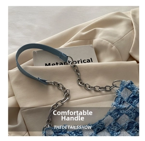 Detail of blue denim checkered crescent bag with frayed edges and chain strap on blazer