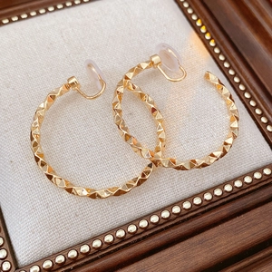 Detail of gold twisted C-shape clip earrings with silicone pads on a vintage background