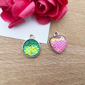 Detail of round green and heart pink fish scale pendants on a rustic wooden table