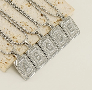 Close-up of five silver square initial pendants with embossed A to E on stone