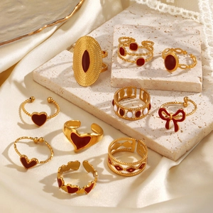 Gold minimalist rings set featuring red heart and bow designs on beige stone surface