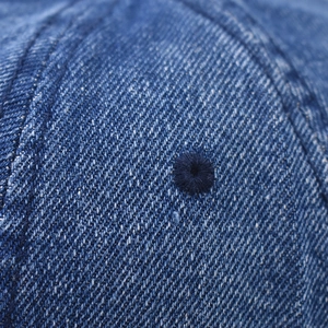 Close-up detail of reinforced eyelet and washed blue denim fabric on the baseball cap