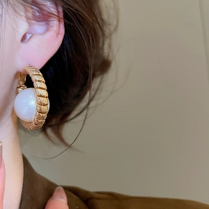 Detail of twisted gold earring featuring a large white pearl on a model's ear
