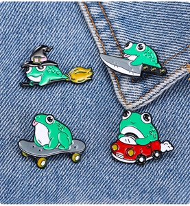 Detail of four green frog enamel pins attached to blue denim jacket fabric