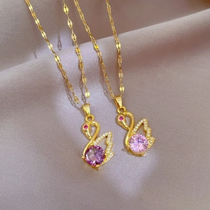 Elegant gold swan necklaces with pink crystals and micro-pavé diamonds on grey fabric
