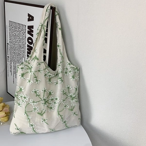 Detailed embroidery of green and white flowers on a white mesh tote bag against a wall