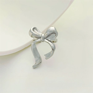 Detailed view of silver bow-shaped ring with textured metallic finish on a white plate