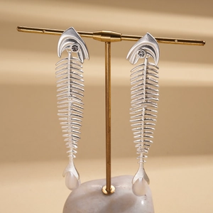Exaggerated silver fishbone earrings with zircon and pearl on a premium display stand