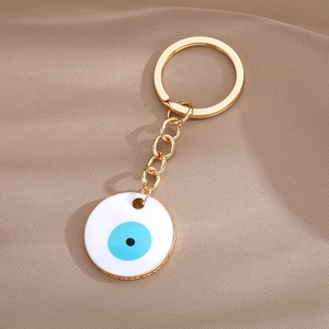 Golden Evil Eye keychain with round blue enamel charm on a textured fabric background