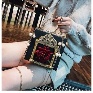 Detail of black box bag with red rose and golden baroque frame with pearl handle
