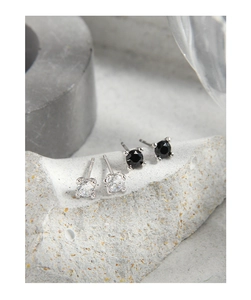 Macro detail of four-prong round zircon stud earrings in silver and black on grey stone
