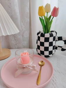 Close-up of pink tulip-shaped soy candle in a glass cup with a decorative ribbon